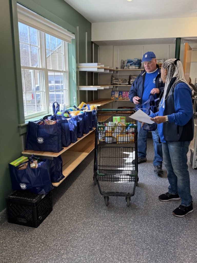Two people stand in front of a row of blue emergency bags that are stocked with food essentials.