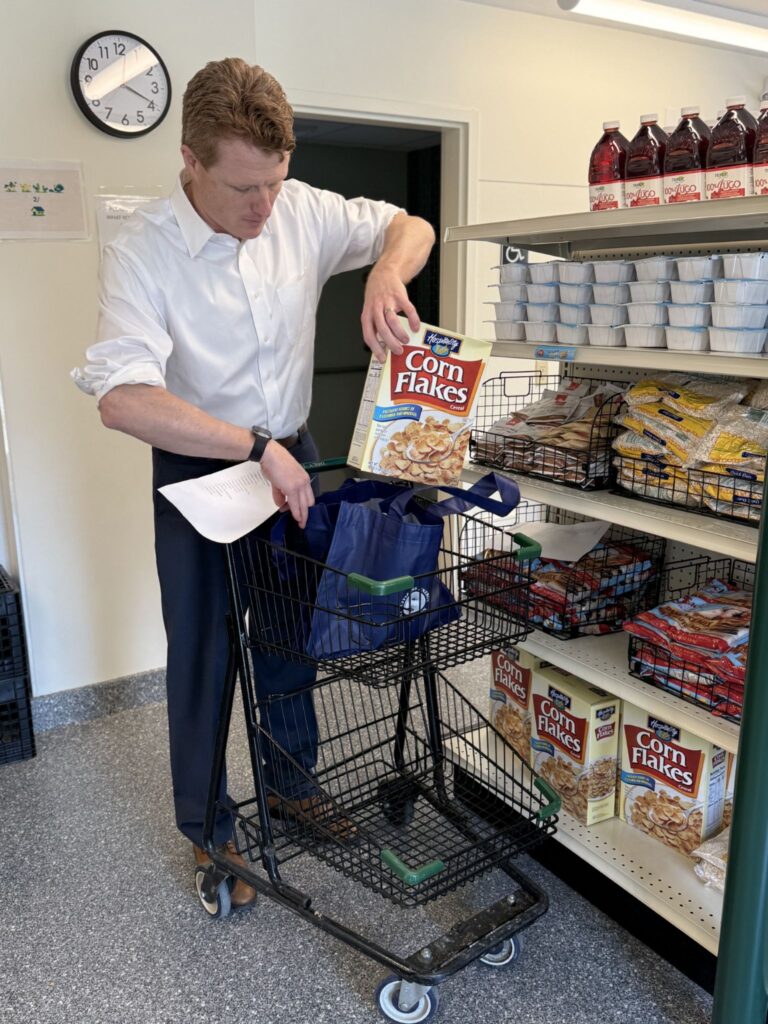 A tall red-headed man with his sleeves rolled up puts a box of cereal in a blue emergency bag.
