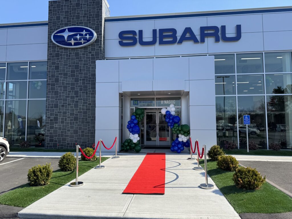 A large white building with the Subaru name and logo. A red carpet, and red velvet ropes welcome guests inside.