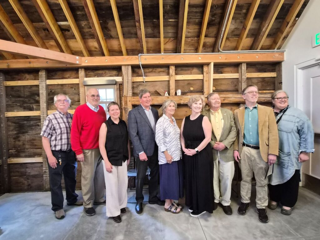 A group of people line up against the bare wooden walls of the Asaph Parlin house.