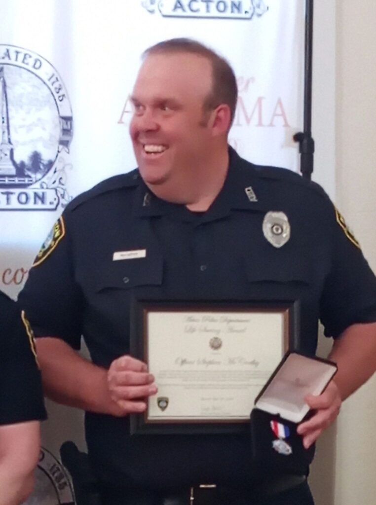 A smiling man in police unform holds a framed citatation while looking at something to his left.