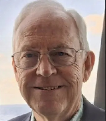 A grey-haired man wtih wire-framed glasses and a sly smile.