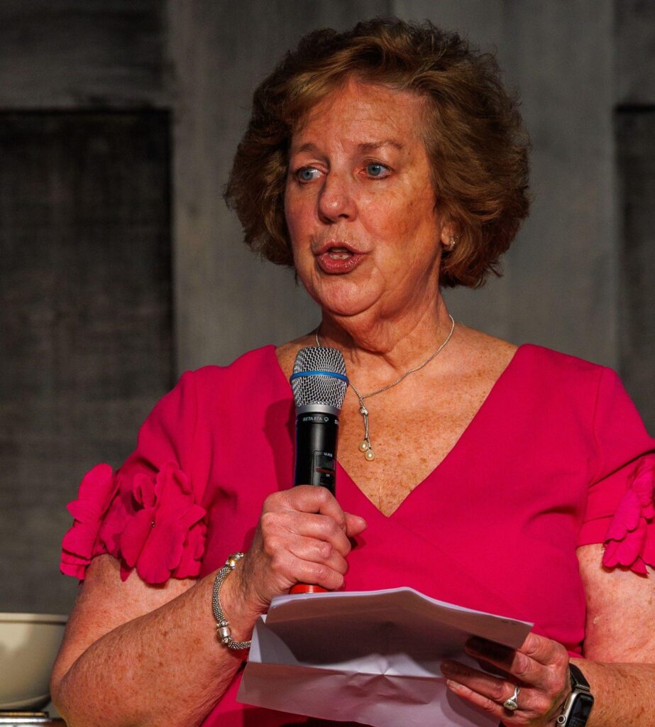 A woman in a red dress speaks into a mic.