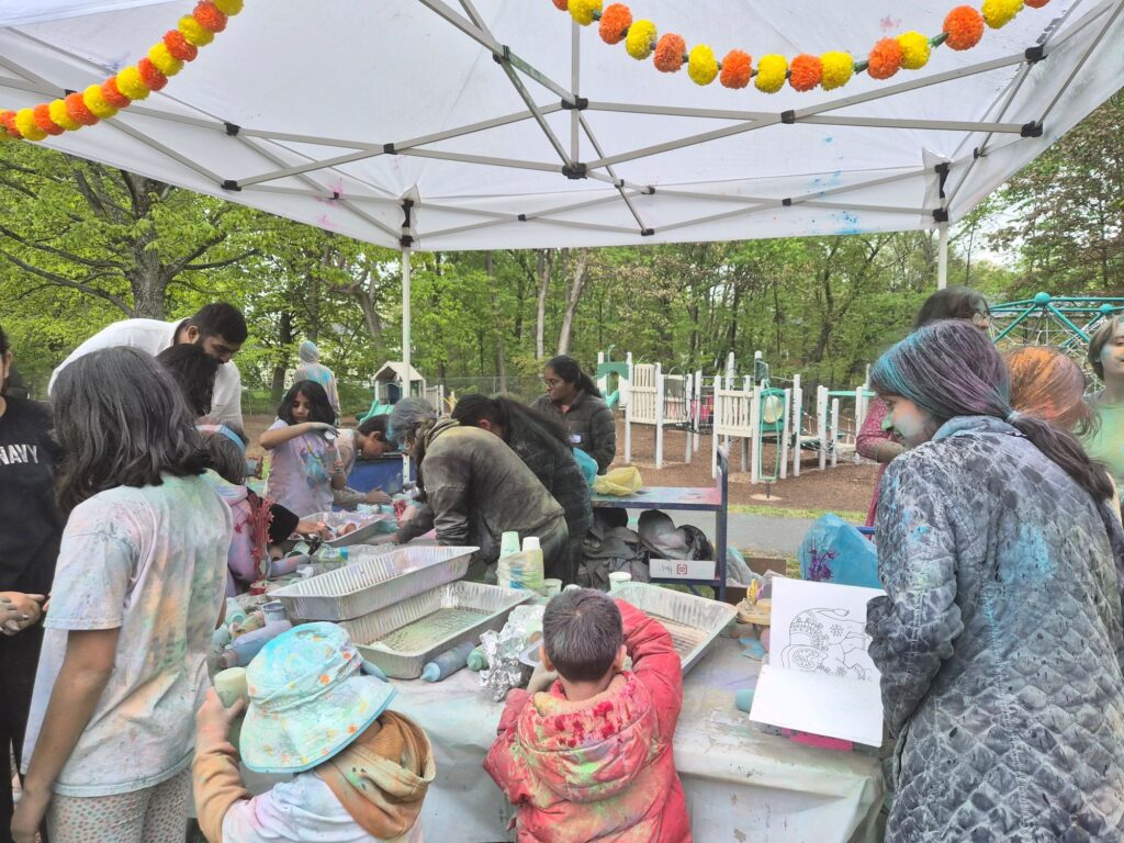 Under the tent, teen girls are filling cups with colored powder. Around the table kids and adults are croweded around picking up new supplides.
