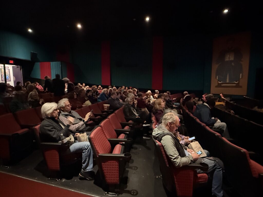 People sitting in a darkened theater waiting for the show to start. Most of the seats are full.