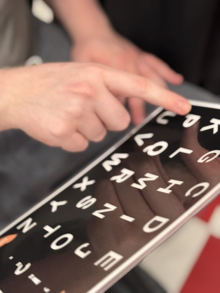 A simple laminated piece of paper with the alphabet in white letters on a black background. A hand is pointing to the letter "P."