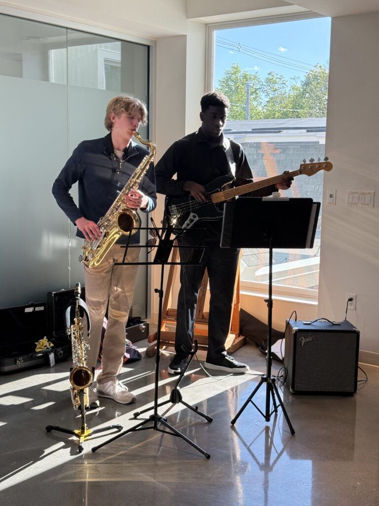 Two young men playing a sax and an electric bass guitar.