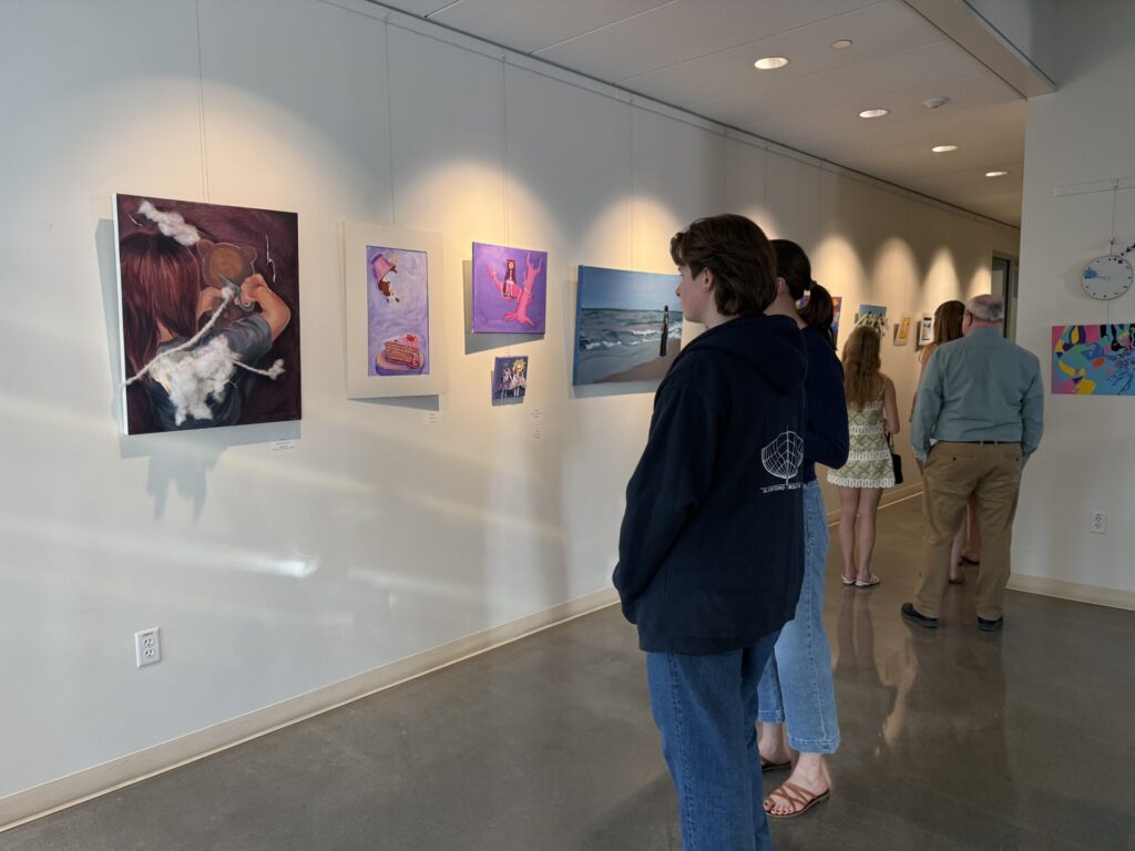On the left, a wall full of pictures by various student artists. On the right, a line of people looking at the art.