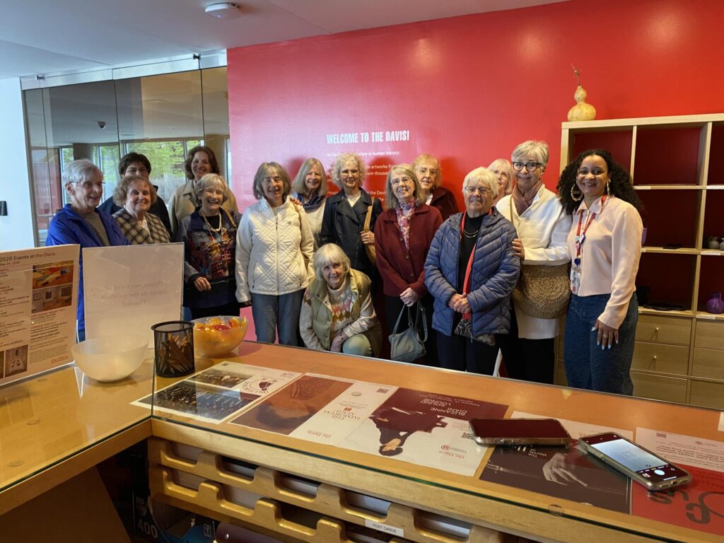 A group of women stand in front of a red-painted wall where you can see the words "Welcome to the Davis!"
