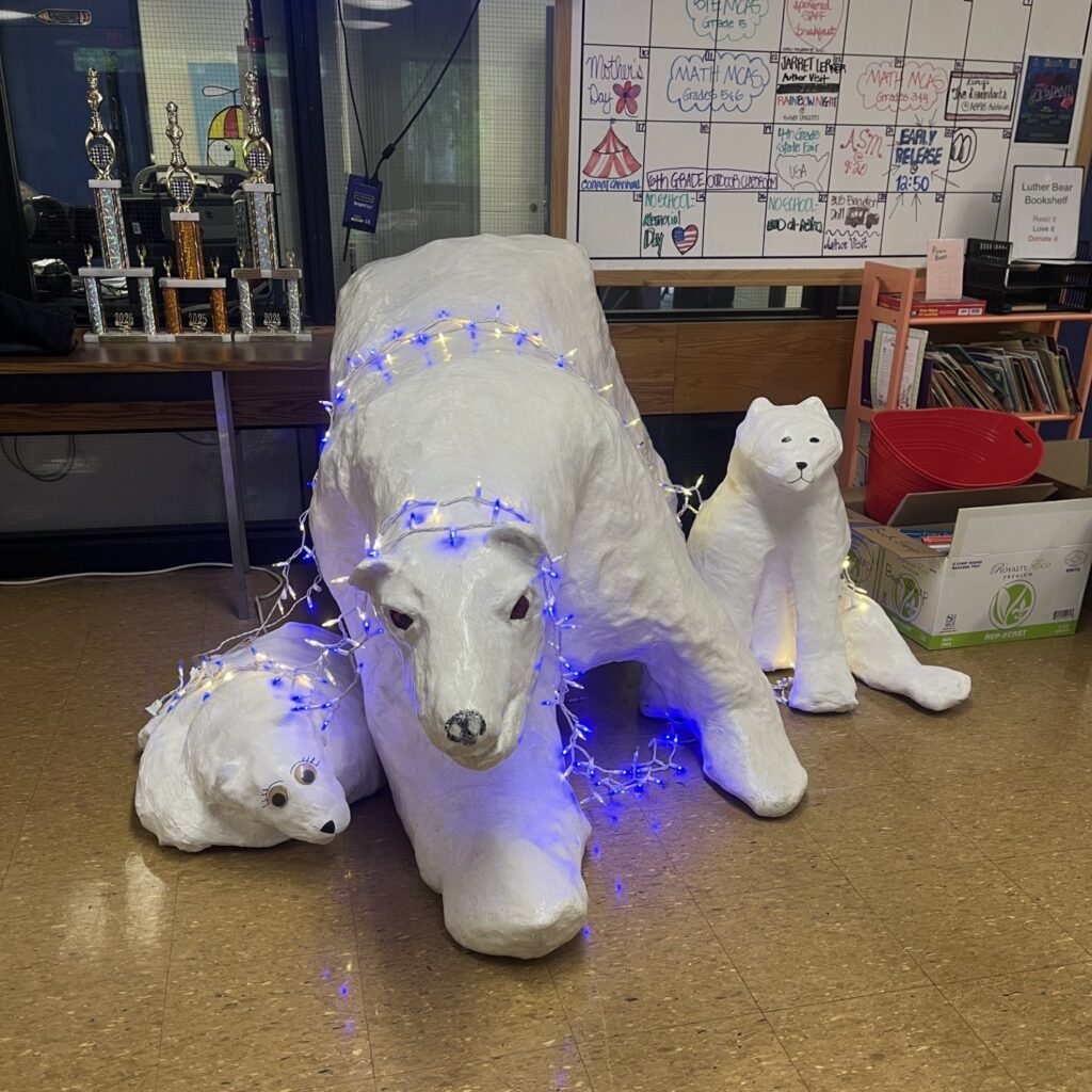 A large polar bear and two cubs in the school lobby. Their fierceness is somewhat mitigated by the blue and white lights draped over the bears and the fact that one bear sports googly eyes and eyelashes.