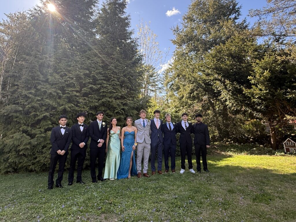A group of mostly boys (and two girls) line up in front of some trees on a lawn. Everyone is dressed up. though at leasst one boy can't seem to move beyond athletic shoes.