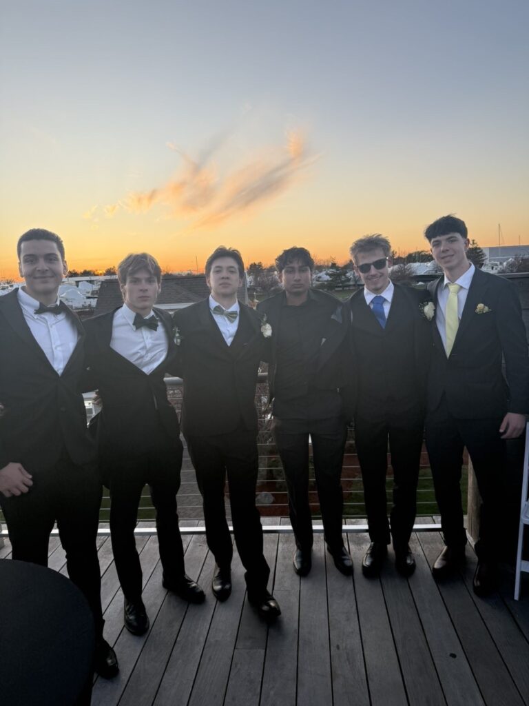 Sunset on a patio (or a boat?). A group of boys, motly in suits and ties pose together.
