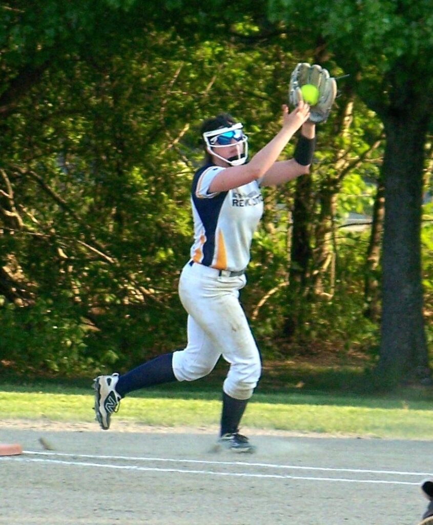 A softbqall player lands with an upraised arm. The ball is in her glove.