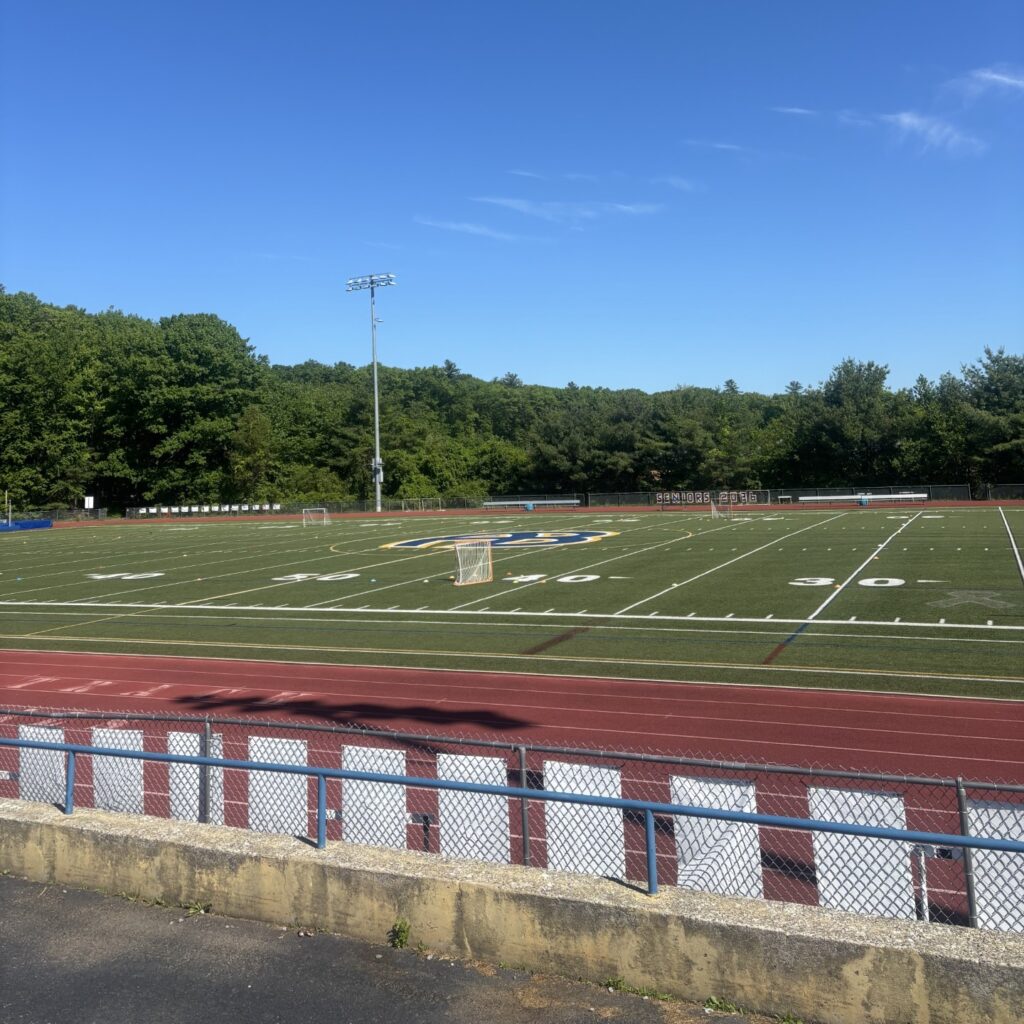 A sports field with the AB logo in the middle and a cinder track in the forefront.