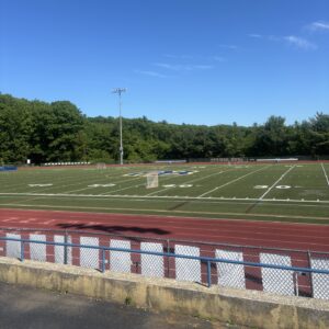 A sports field with the AB logo in the middle and a cinder track in the forefront.