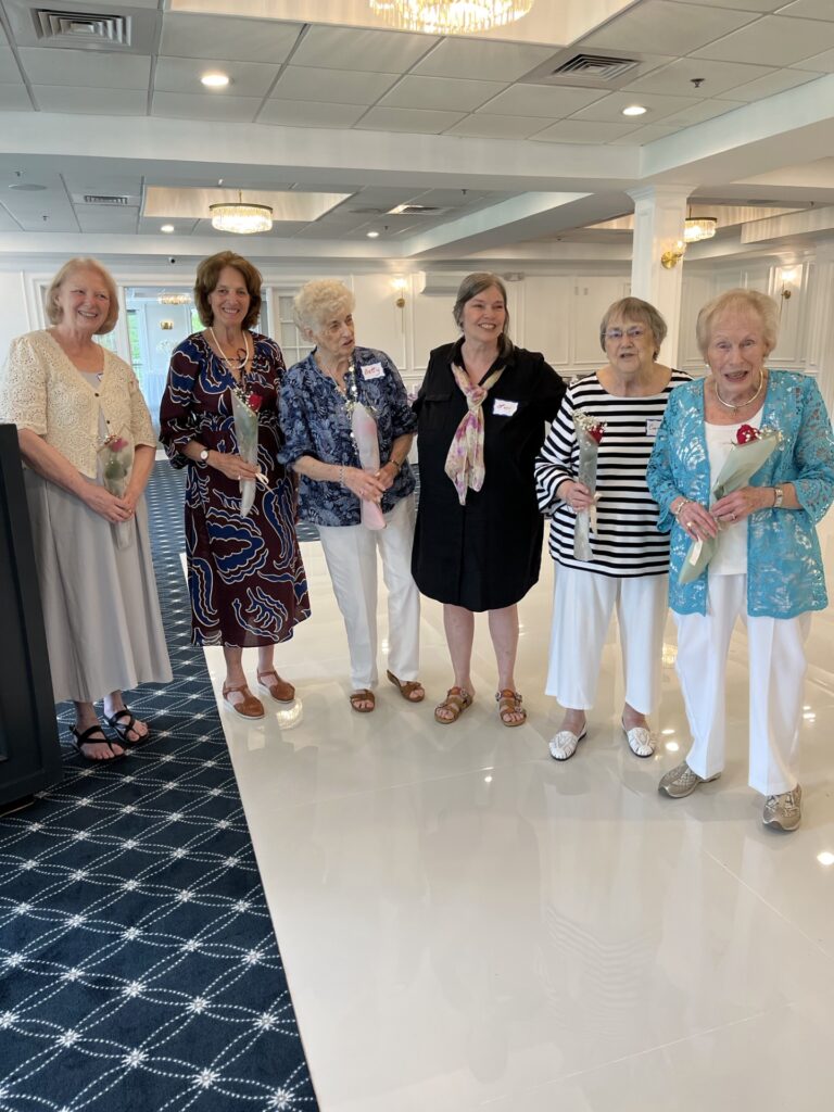 A group of women, mostly older, stand in a white room.
