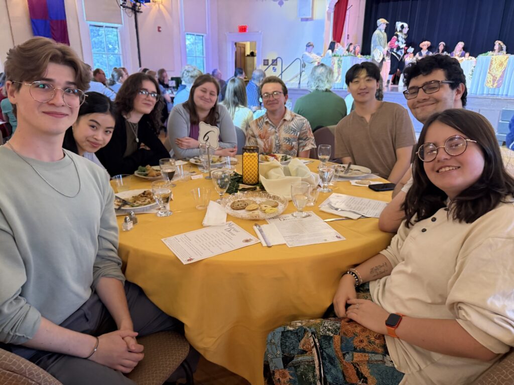 A table full of young adults smile at the camera.