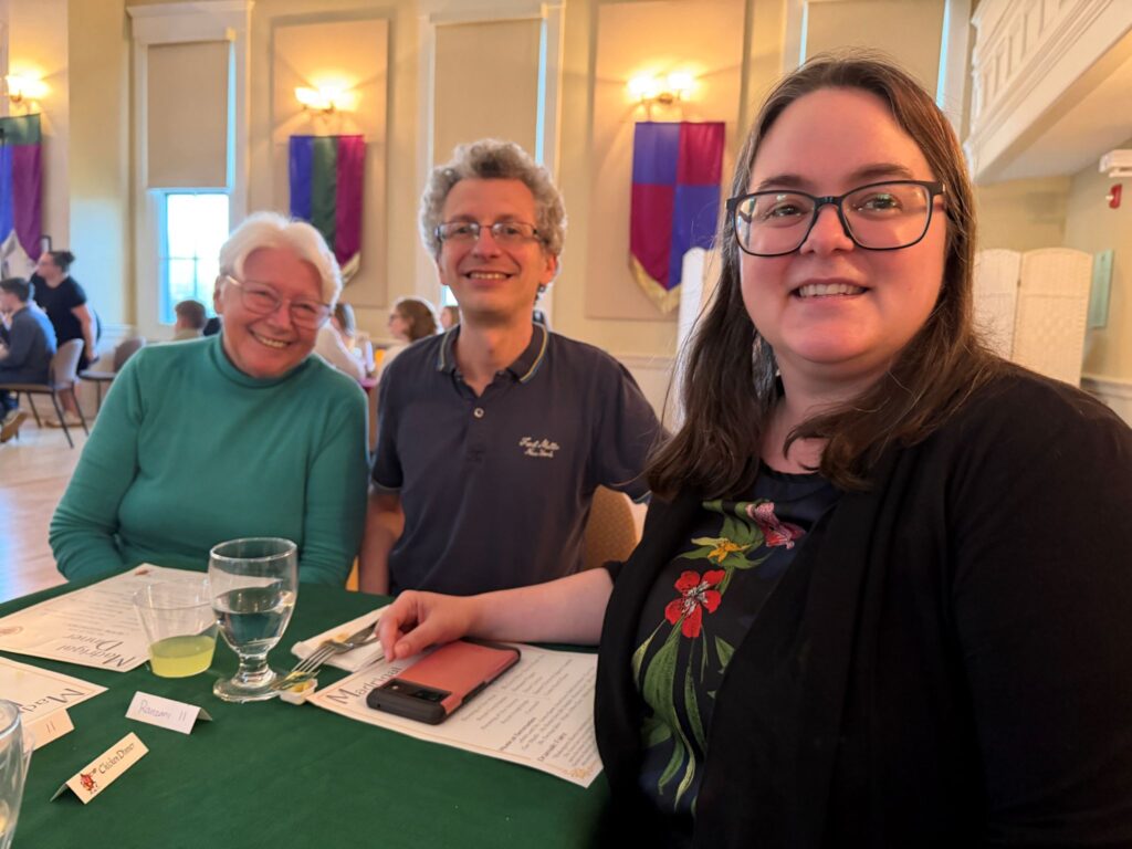 A smiling woman with short white hair and a green sweater, a man in a polo shirt, and a woman in a flowered shirt.