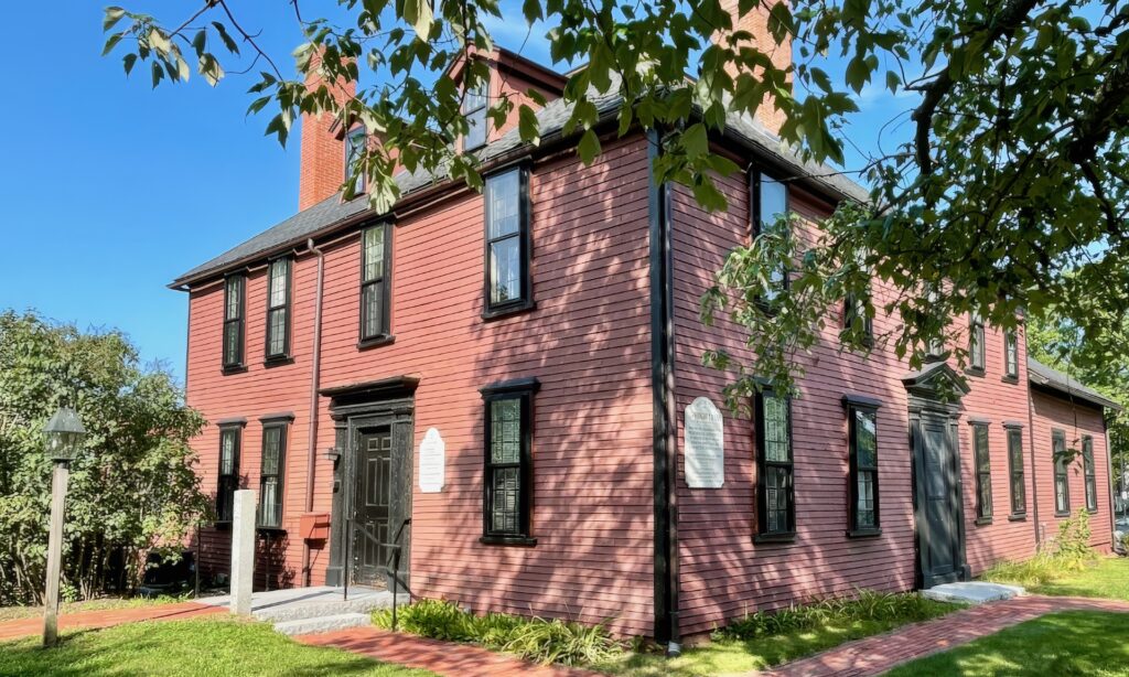 A red wooden Colonial-era building on a sunny day.
