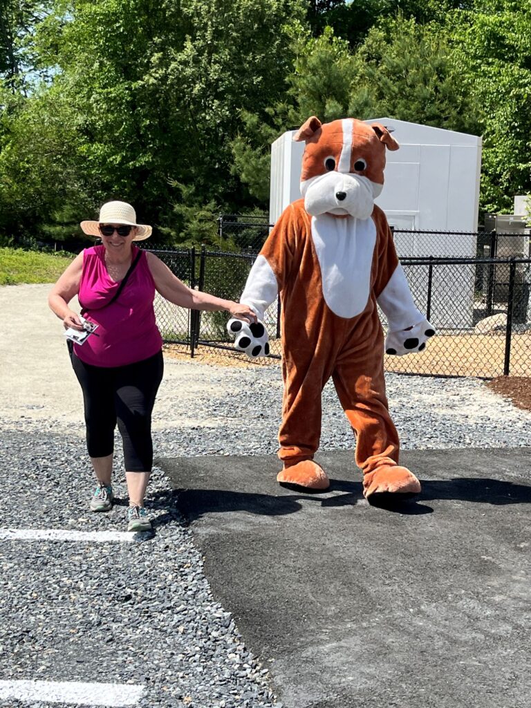 A woman wearing a straw hat and pink shirt walks hand in hand with a person in a borown and white dog costume.