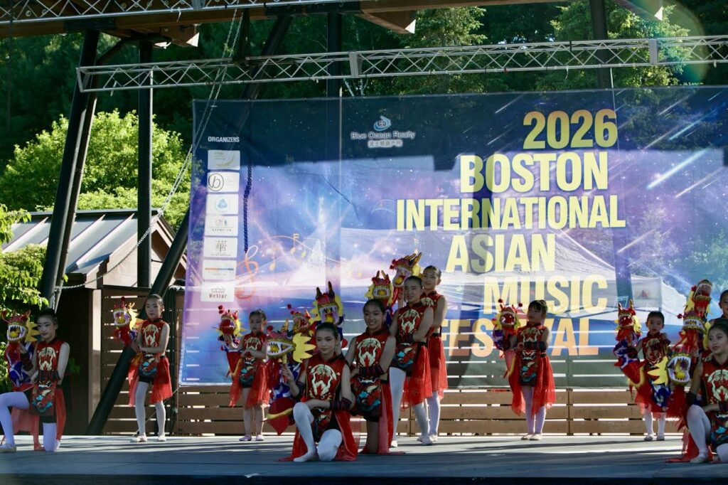Children in red, black, and white costumes pose at the end of a dance. Most of the children are holding small stuffed dragons, which they used to great effect during the dance.