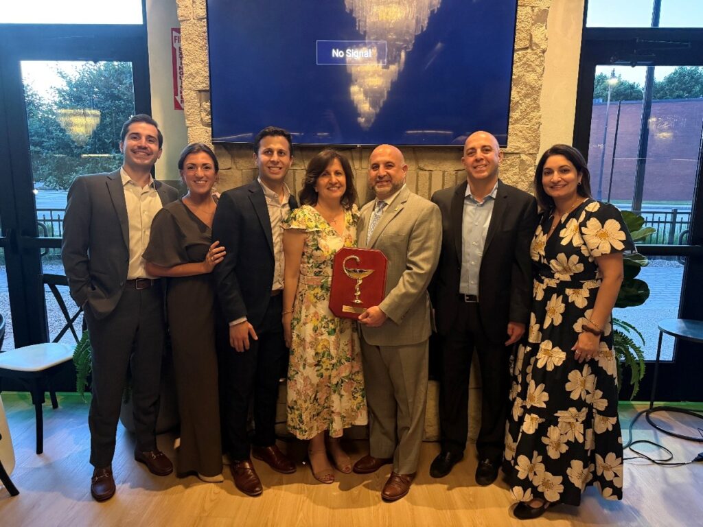 In the middle of the photo a balding man in a suit holds a plaque that has a stemmed bowl. Surrounding him are several other people who look related.