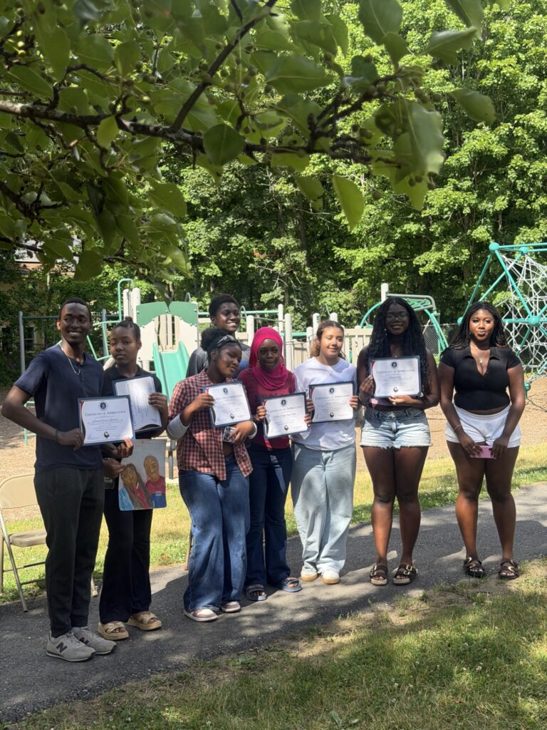A group of students stands in front of a playground holding certificates.