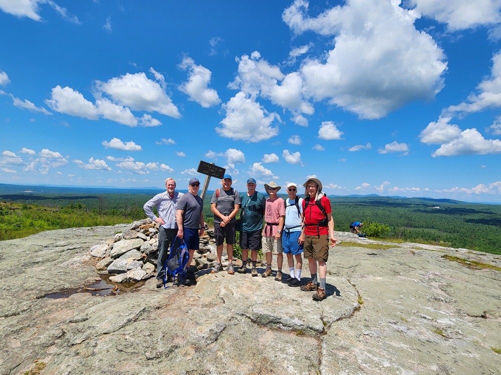 Hikers posing at the summit of Blue Job Mountain in New Hampshire with a sign in the background.