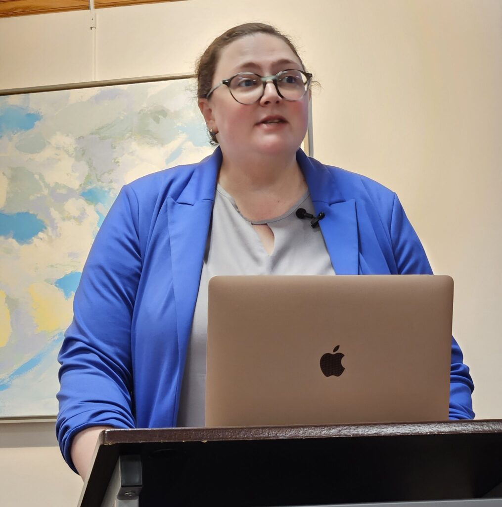 Emily Sneff standing at a podium with a laptop open in front of her at Acton Memorial Library.