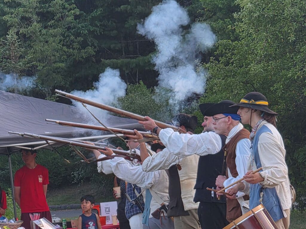 A drummer and people shooting rifles wearing Revolution Era costumes at Nara Park in Acton.