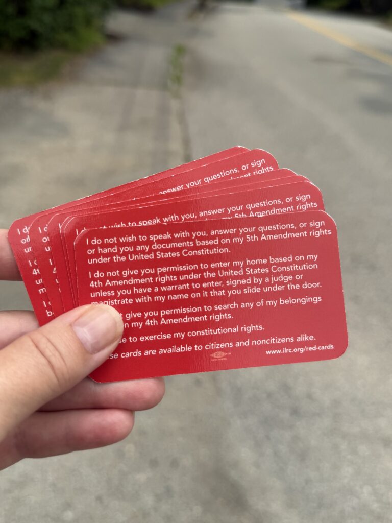A hand holding a fanned out stack of red cards with information from the Legal Resource Center on the rights of immigrants in English language.